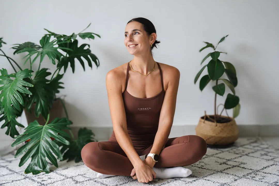 Carla sitting cross-legged on the floor at home, smiling as she looks to one side